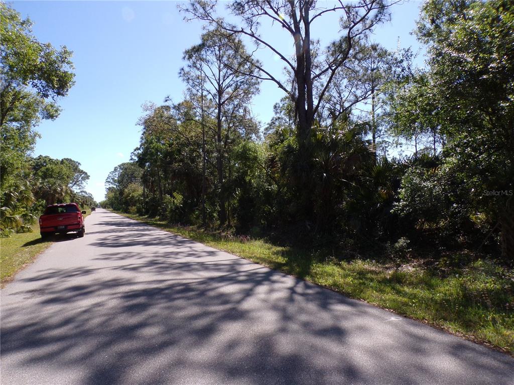 A red pickup truck is parked on the shoulder of a paved road near trees — 26215 CUSTER ROAD, PUNTA GORDA, FL