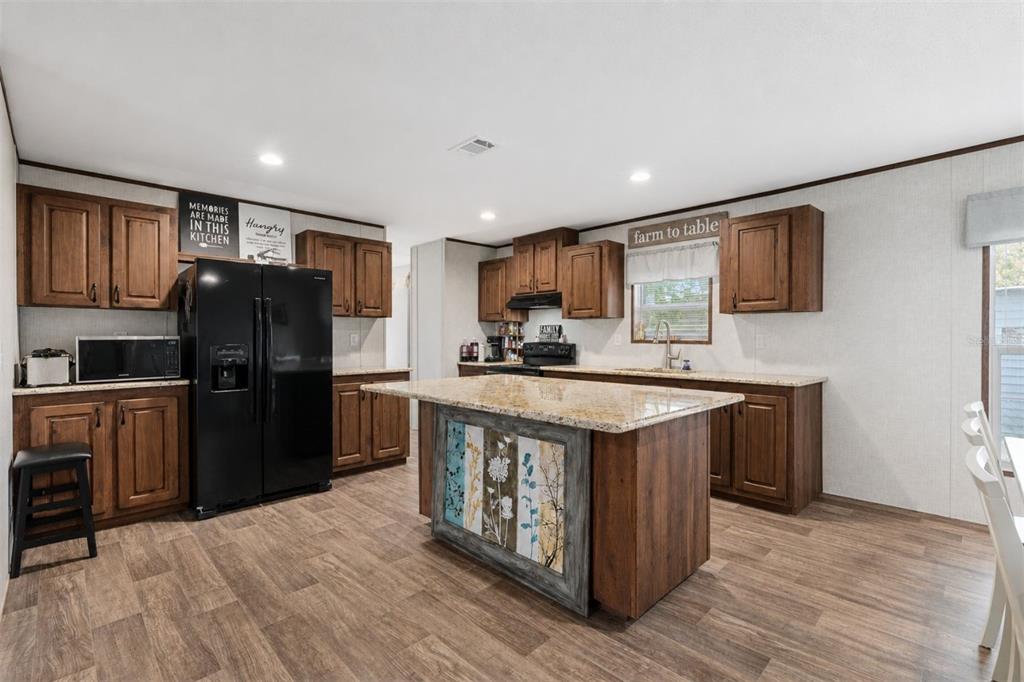 A kitchen features wood cabinets, granite countertops, a central island, and a black refrigerator — 42215 BEECH AVENUE, DELAND, FL