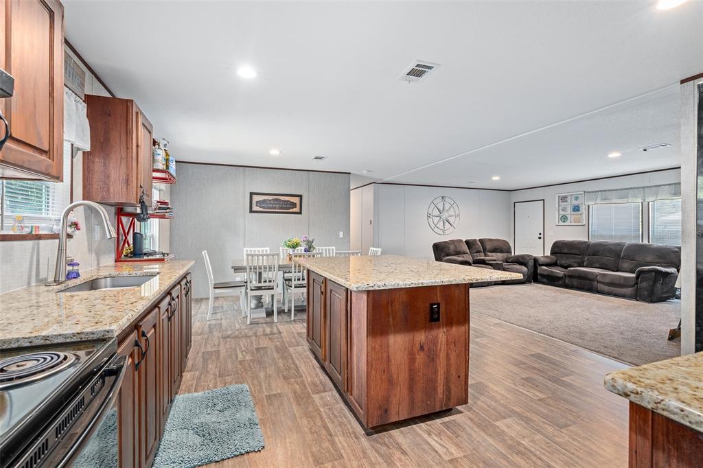 A kitchen with granite countertops and wood cabinets opens into a dining and living area — 42215 BEECH AVENUE, DELAND, FL