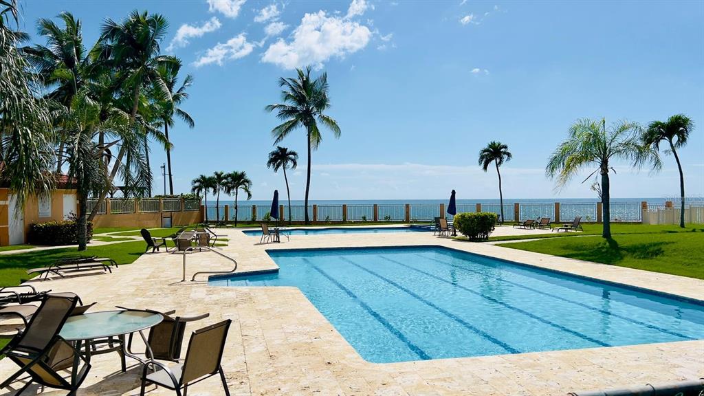 A swimming pool with lounge chairs sits on a patio overlooking the ocean and palms — 3 CARR 115 PLAYA ALMIRANTE UNIT PH 605B, ANASCO, PR