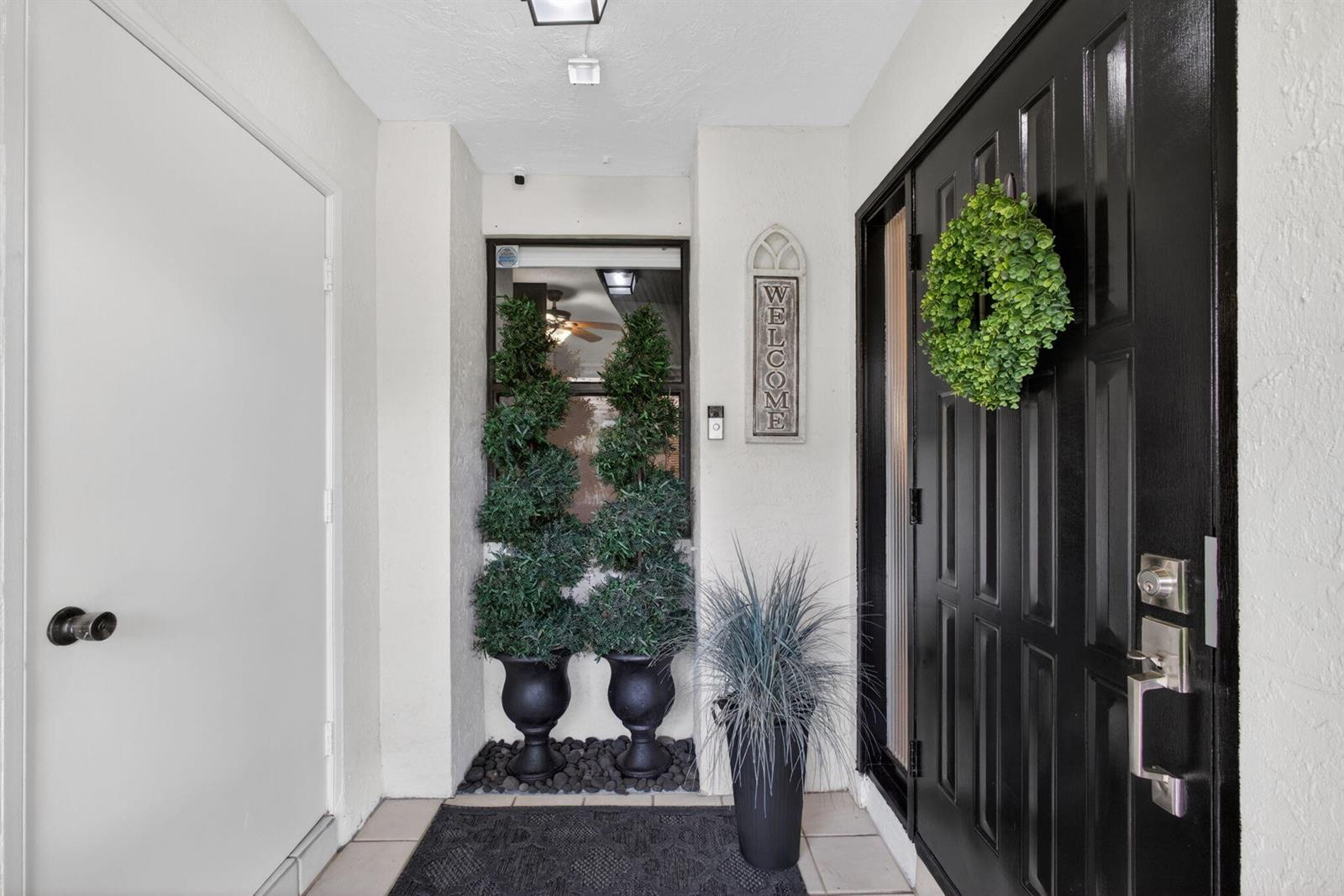 A black front door with a wreath stands next to two potted topiary plants — 101 Half Moon Circle # C, Jupiter FL 33458, JUPITER, FL