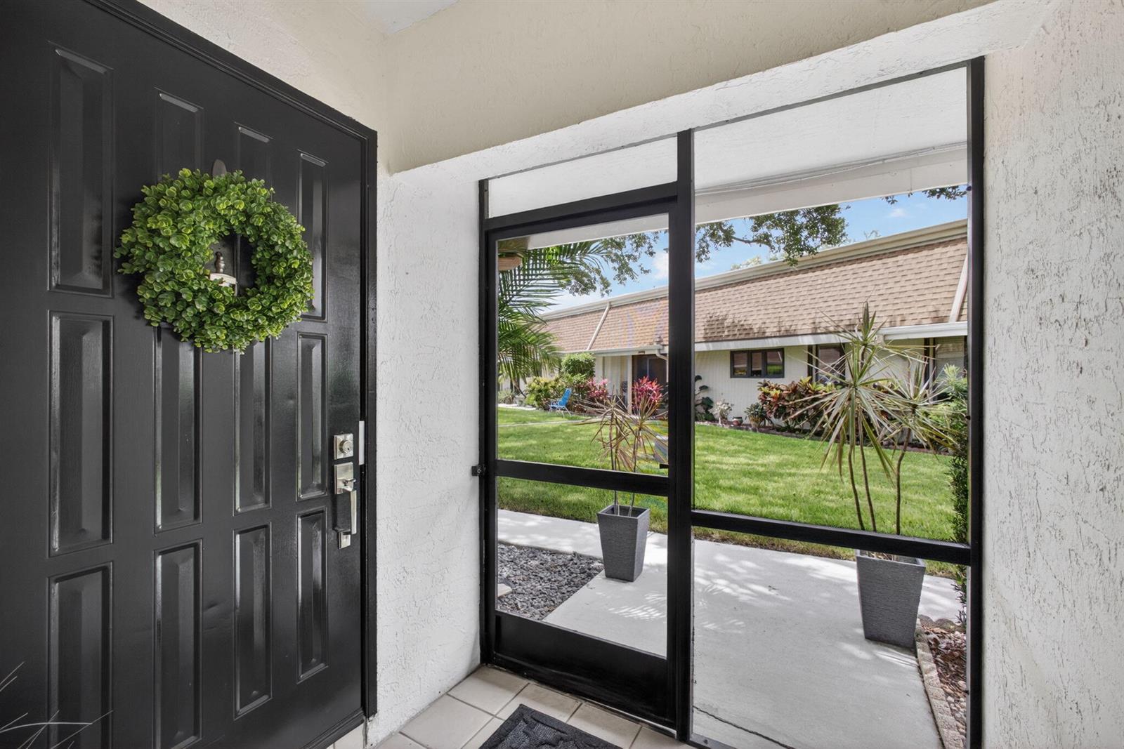 A black front door with a wreath opens to a screened entryway facing a lawn — 101 Half Moon Circle # C, Jupiter FL 33458, JUPITER, FL