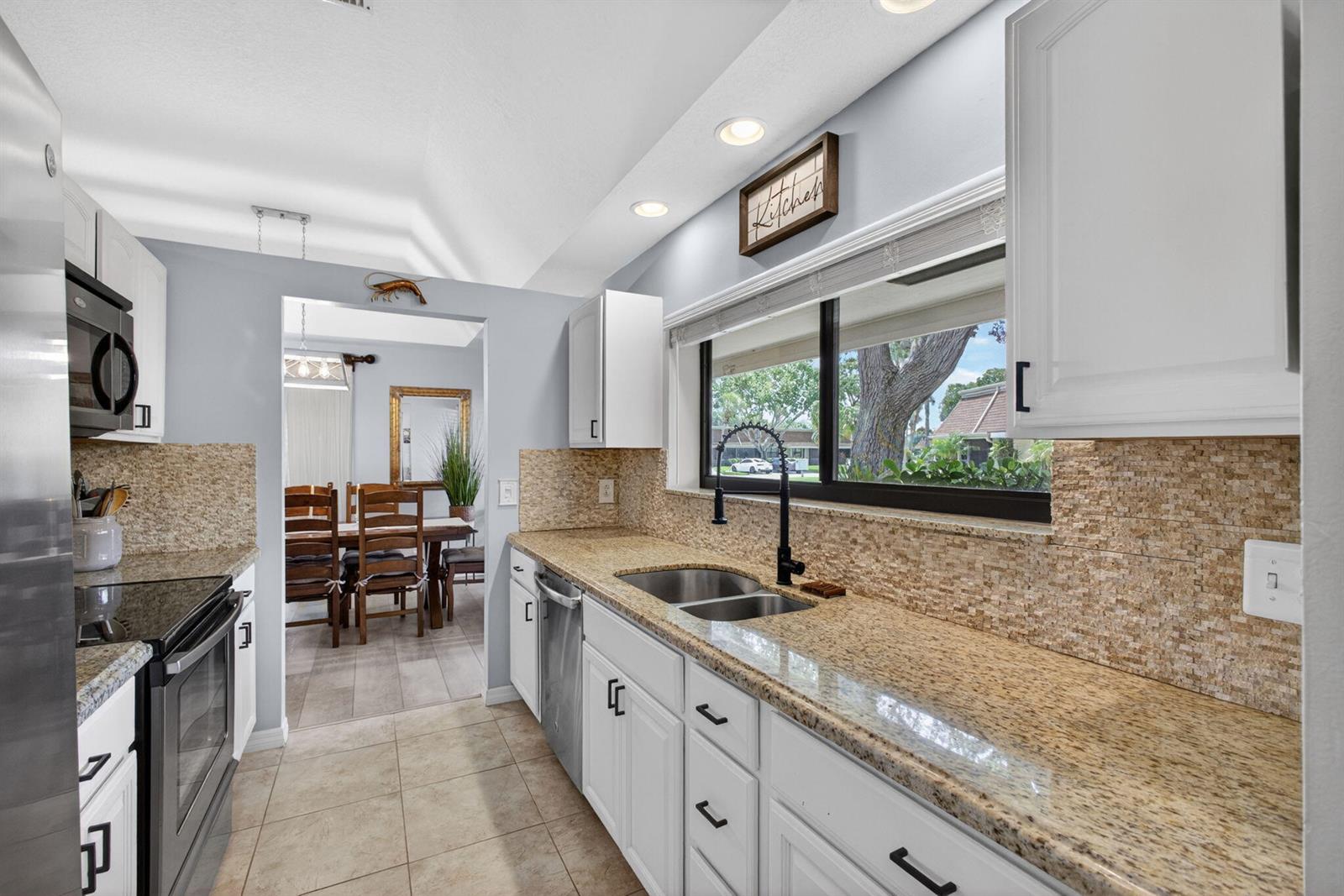 A kitchen features white cabinets, granite countertops, a tile backsplash, and a view into a dining room — 101 Half Moon Circle # C, Jupiter FL 33458, JUPITER, FL