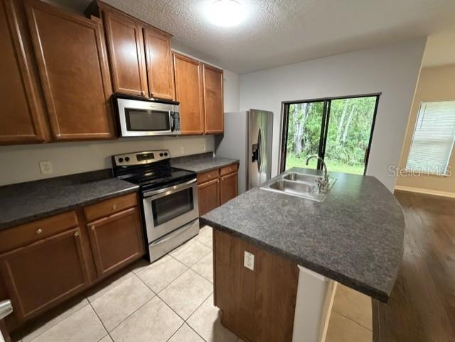 A kitchen features wood cabinets, stainless steel appliances, a center island, and tile flooring — 6025 APOLLOS CORNER WAY, ORLANDO, FL