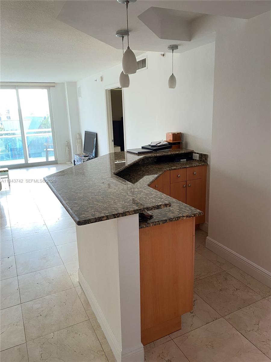 A kitchen features a granite-topped peninsula, light wood cabinets, and tile flooring — 6917 Collins Ave # 426, Miami Beach FL 33141, MIAMI BEACH, FL