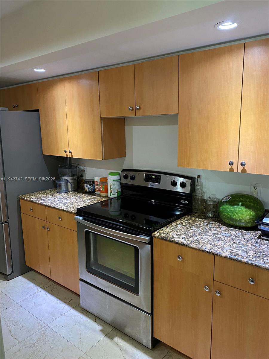 A kitchen features light wood cabinets, granite countertops, and stainless steel appliances — 6917 Collins Ave # 426, Miami Beach FL 33141, MIAMI BEACH, FL