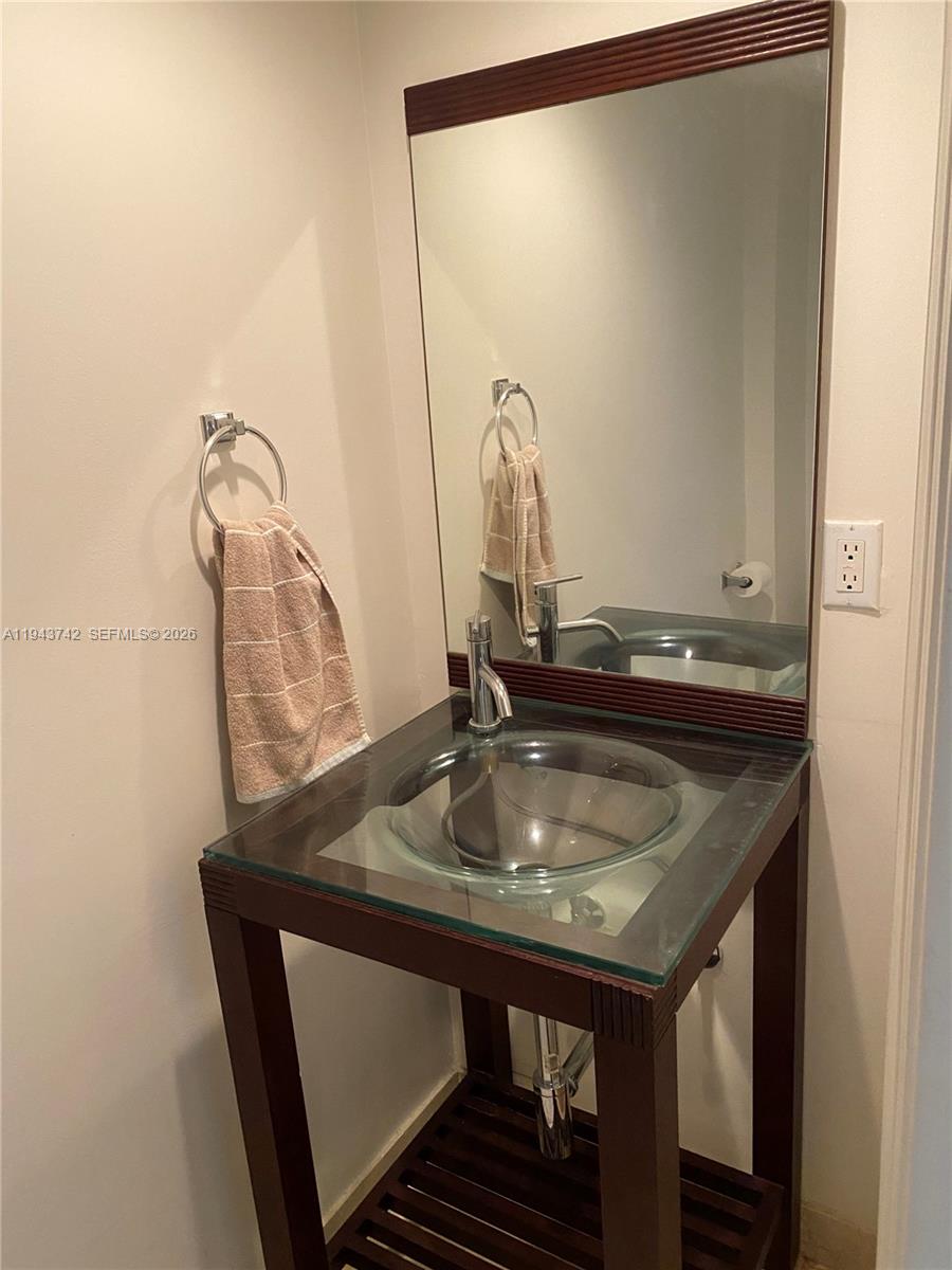 A bathroom features a glass vessel sink on a dark wood vanity with a mirror — 6917 Collins Ave # 426, Miami Beach FL 33141, MIAMI BEACH, FL