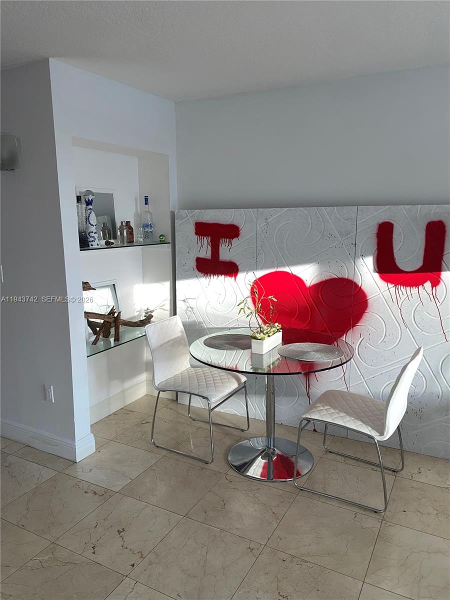 A dining area features a glass table, two white chairs, and wall art with a heart — 6917 Collins Ave # 426, Miami Beach FL 33141, MIAMI BEACH, FL