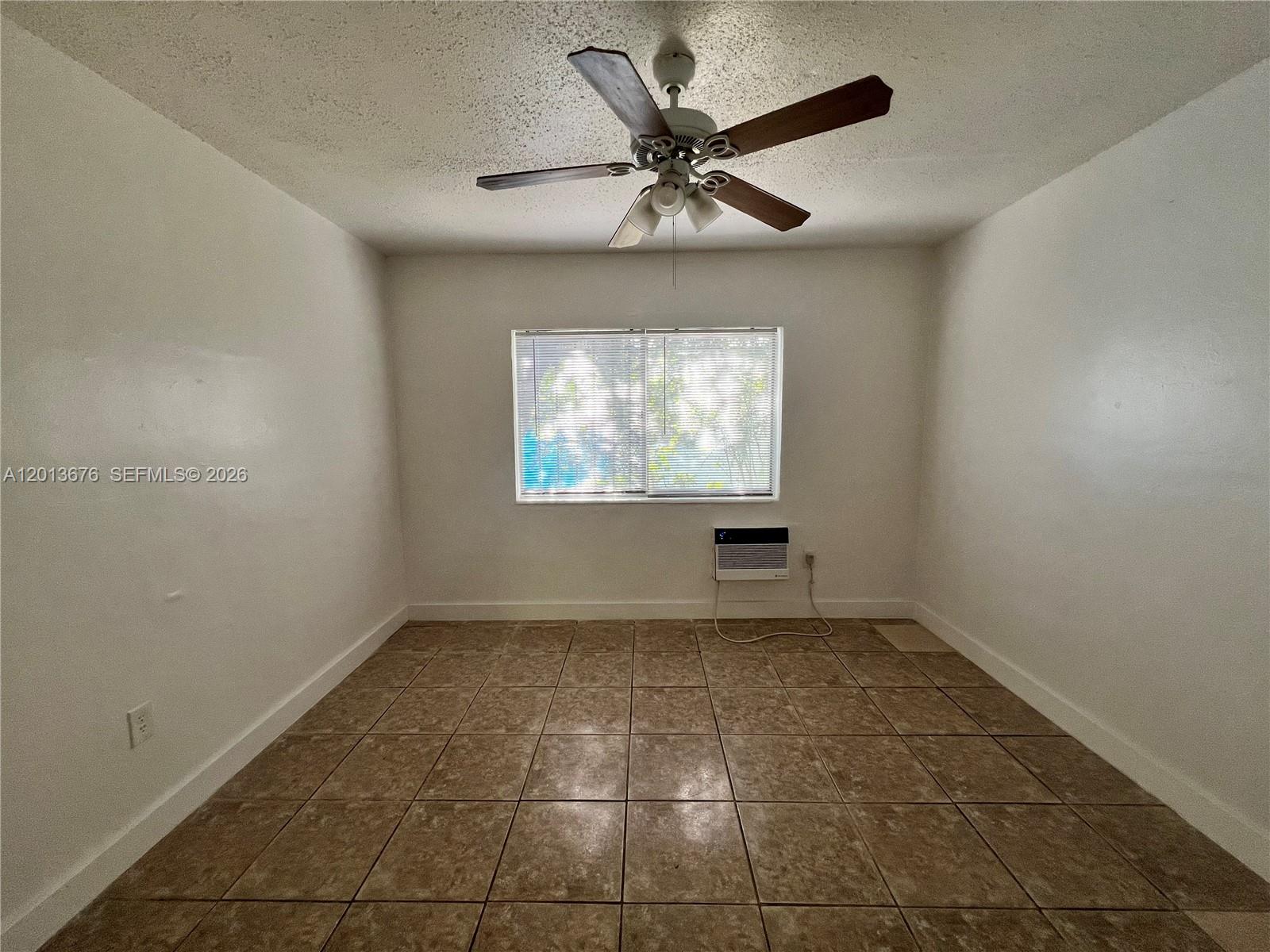 An empty room features white walls, tan tile flooring, a ceiling fan, and a window unit — 5600 NE 1st Ave # 2, Miami FL 33137, MIAMI, FL