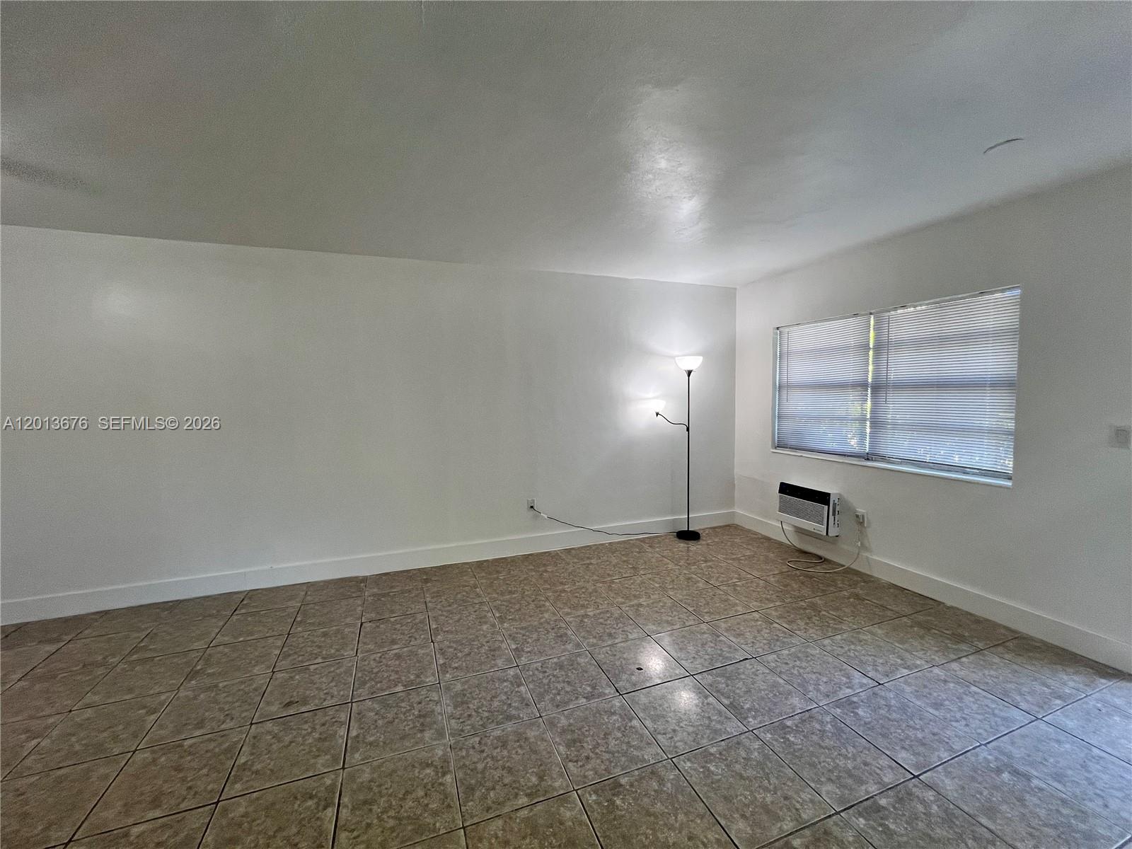 An empty room features white walls, tiled floors, a floor lamp, and a window unit — 5600 NE 1st Ave # 2, Miami FL 33137, MIAMI, FL