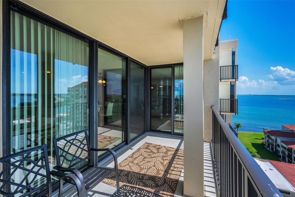 A balcony with metal furniture and a rug overlooks the ocean and nearby buildings — 6322 PALMA DEL MAR BOULEVARD S UNIT 1104, ST PETERSBURG, FL