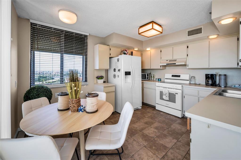 A kitchen with white appliances and cabinets, tile flooring, and a round dining table — 6322 PALMA DEL MAR BOULEVARD S UNIT 1104, ST PETERSBURG, FL
