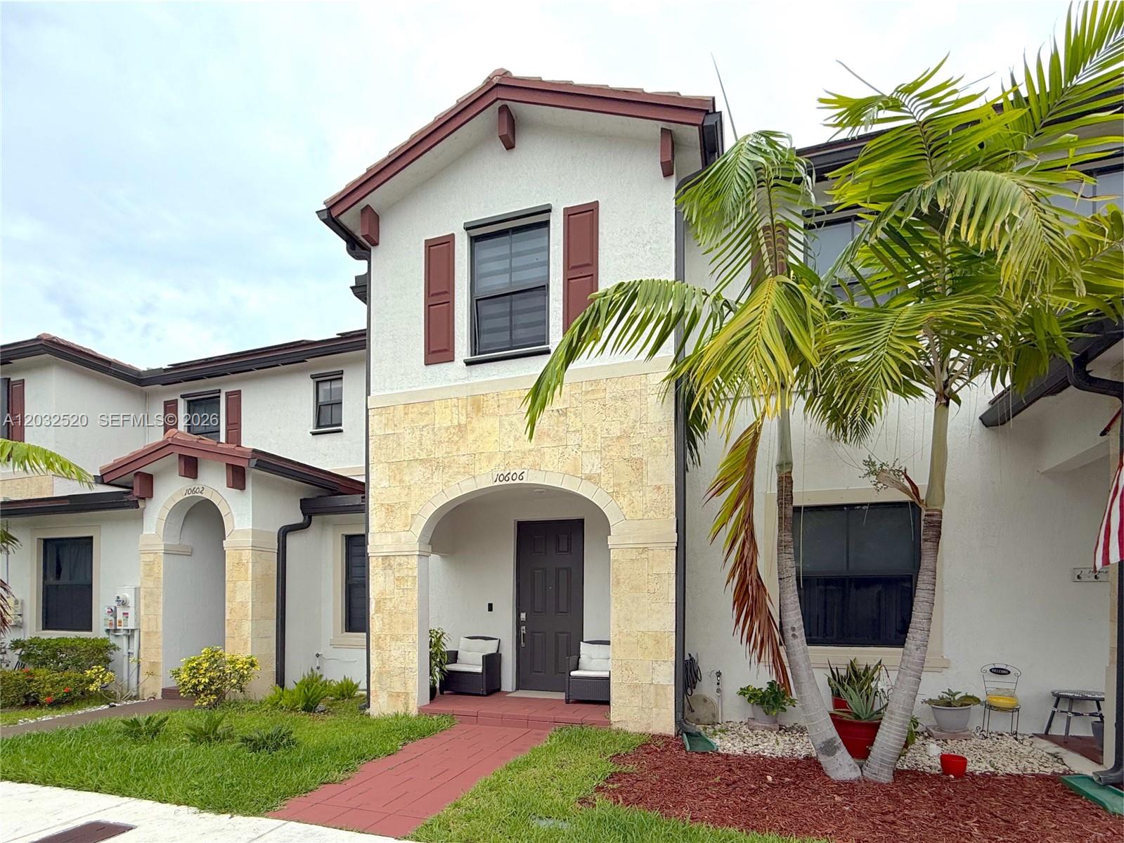 The exterior of a two-story townhouse features a stone-arched entryway, red shutters, and palm trees — 10606 W 32nd Ln, Hialeah FL 33018, HIALEAH, FL