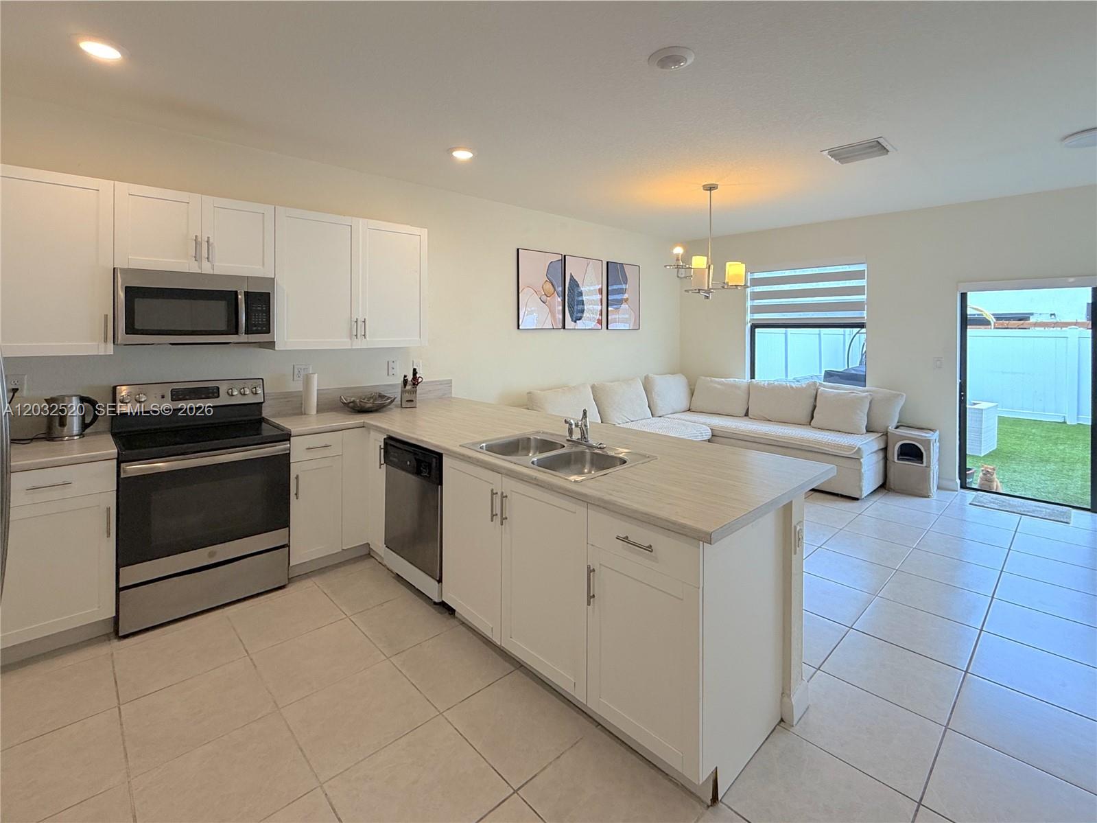 A kitchen with white cabinets and stainless steel appliances opens to a living area — 10606 W 32nd Ln, Hialeah FL 33018, HIALEAH, FL