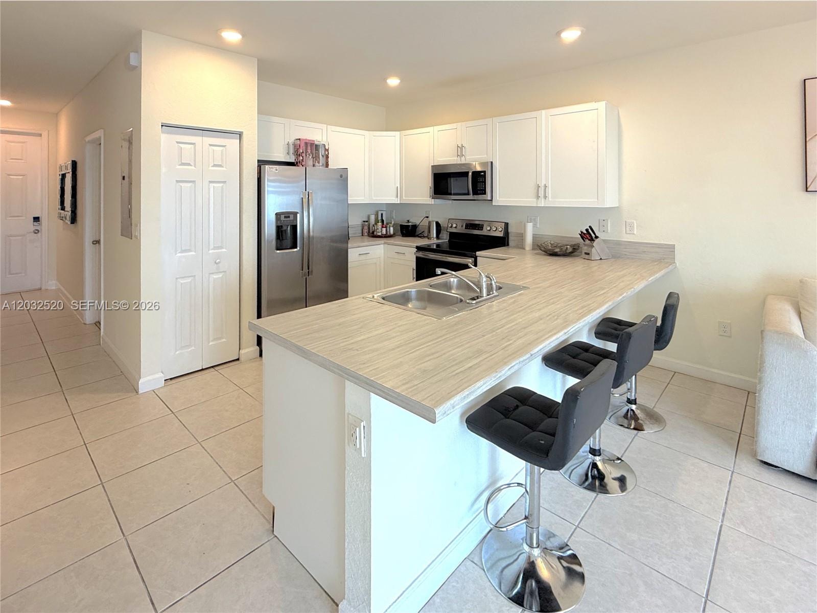 A kitchen features white cabinets, stainless steel appliances, and a wood-look countertop island with stools — 10606 W 32nd Ln, Hialeah FL 33018, HIALEAH, FL