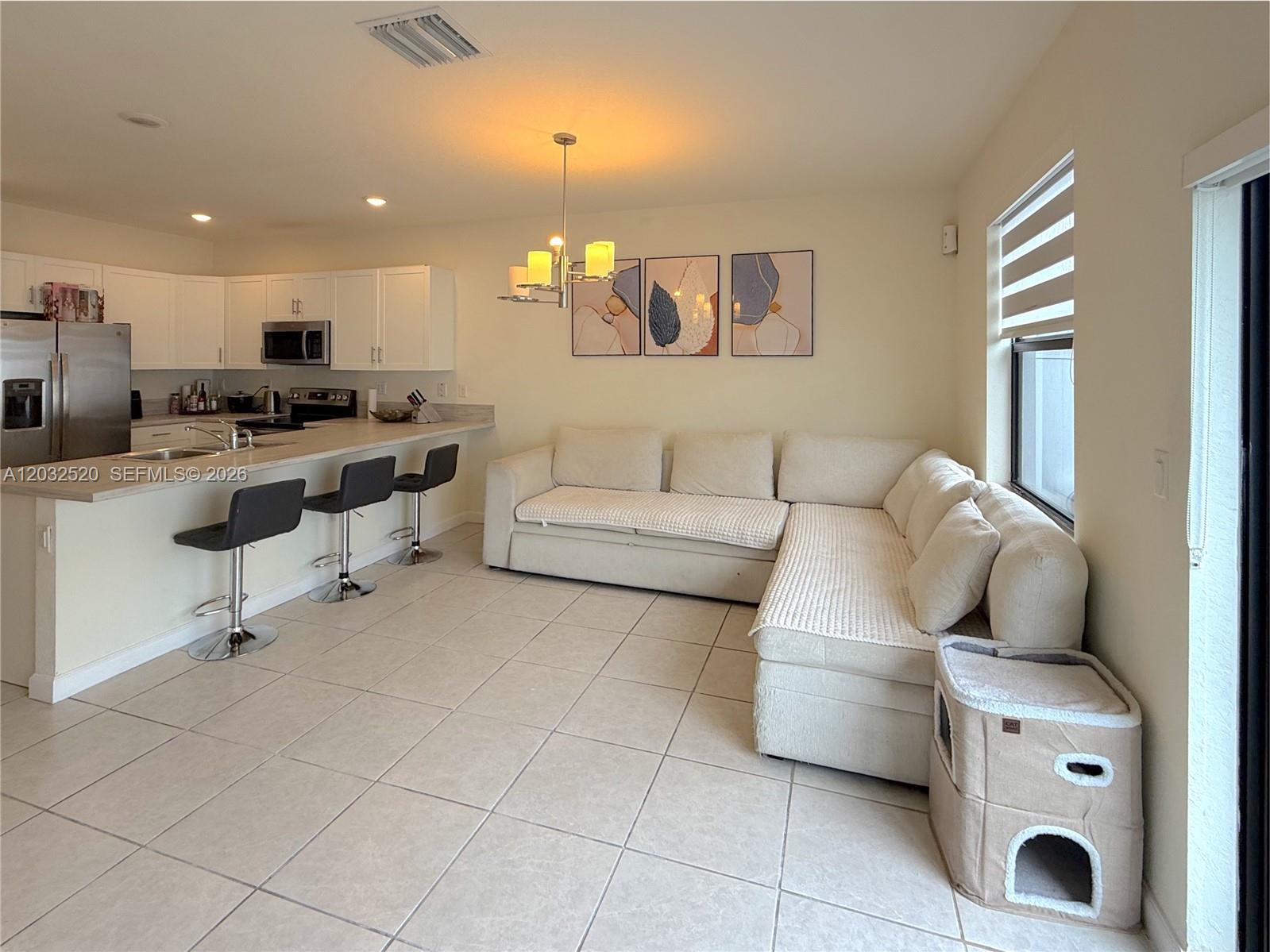 An open-concept kitchen with a breakfast bar overlooks a living area with a sectional sofa — 10606 W 32nd Ln, Hialeah FL 33018, HIALEAH, FL