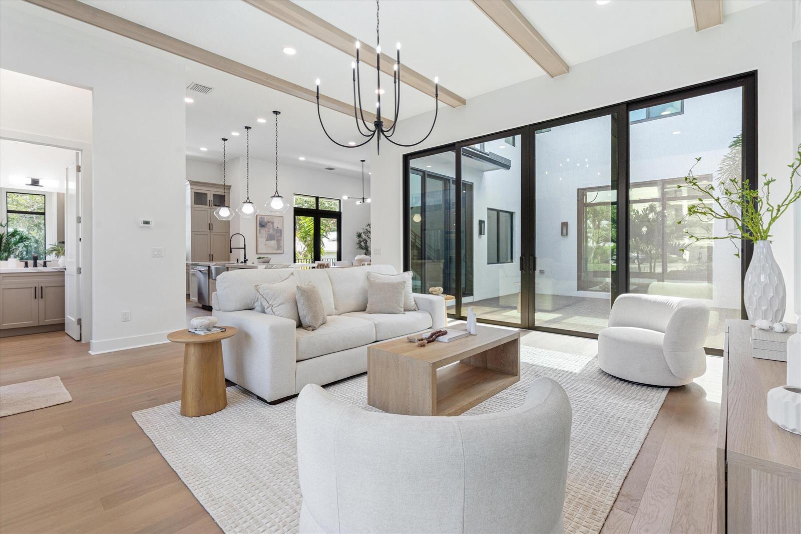 A bright living room features a white sofa, two armchairs, wood beams, and large glass doors — 432 NW North River Drive, Stuart FL 34994, STUART, FL