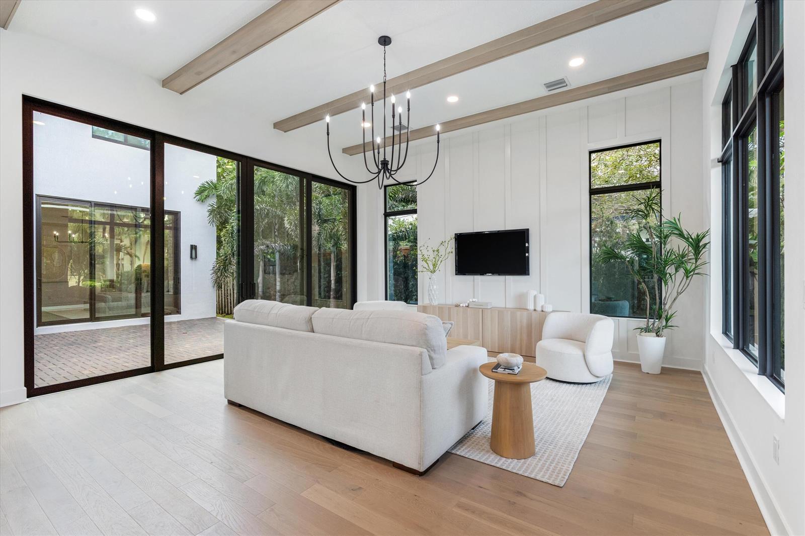 A bright living room features light wood floors, exposed ceiling beams, and large glass sliding doors — 432 NW North River Drive, Stuart FL 34994, STUART, FL
