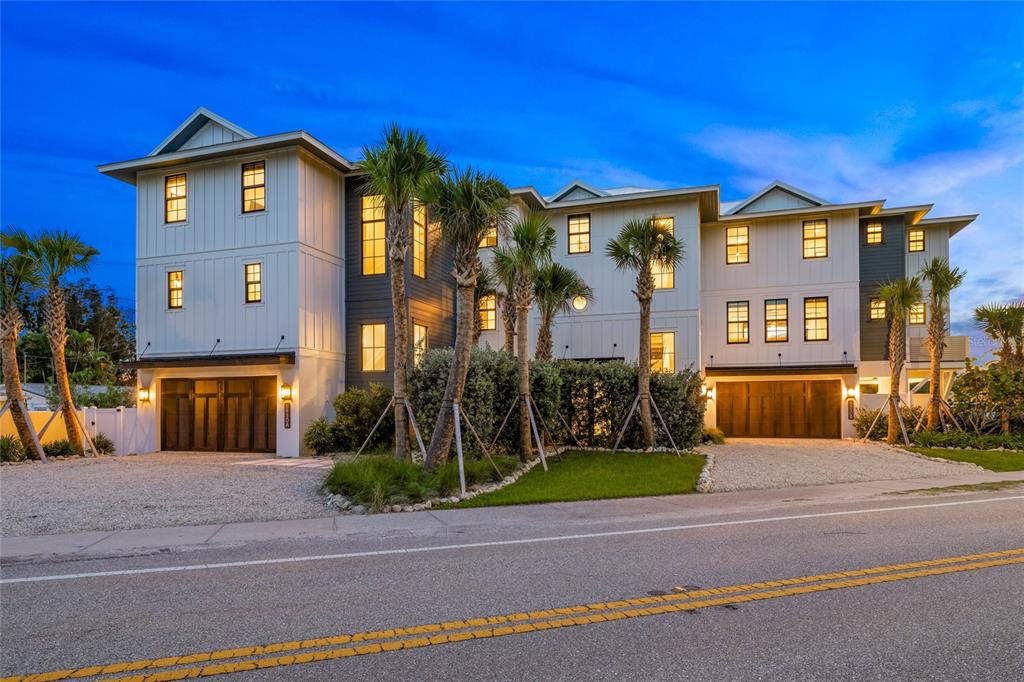 A three-story modern residential building with white siding, dark accents, and two ground-level garages — 6910 MIDNIGHT PASS ROAD UNIT A, SARASOTA, FL