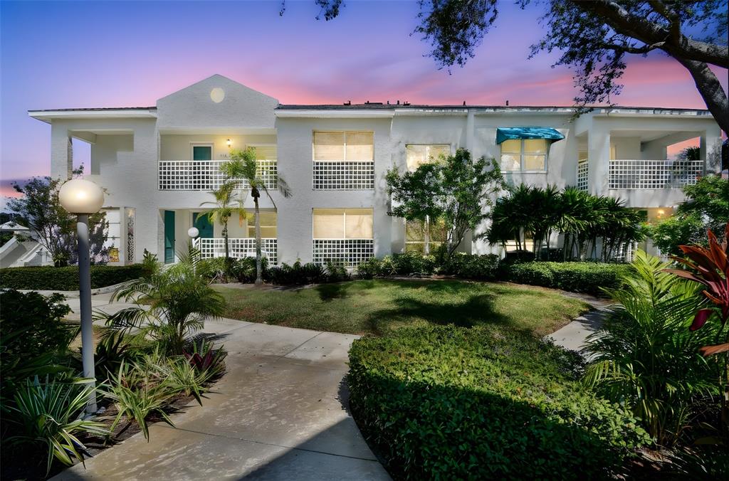 A two-story white apartment building with balconies, a landscaped lawn, and a paved walkway — 318 108TH STREET W UNIT 106, BRADENTON, FL