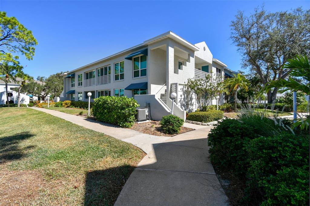A two-story apartment building features white stucco walls, blue window awnings, and concrete walkways — 318 108TH STREET W UNIT 106, BRADENTON, FL