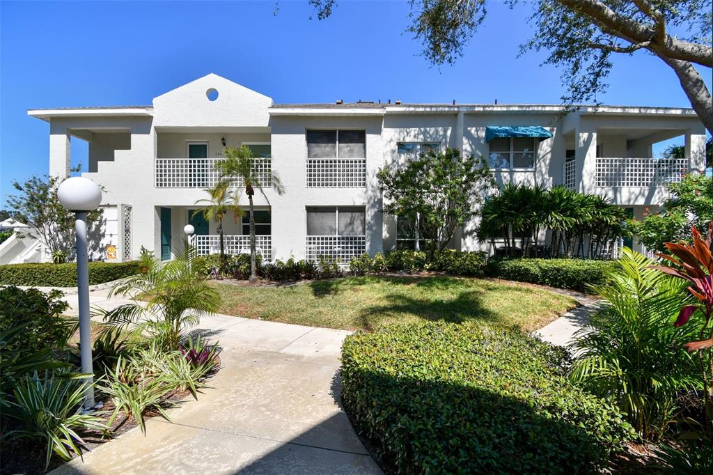 A two-story apartment building with white stucco walls, balconies, and a landscaped courtyard — 318 108TH STREET W UNIT 106, BRADENTON, FL