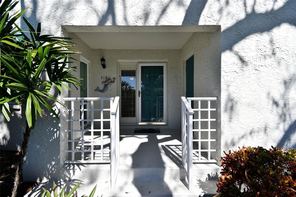 The exterior entrance features a white stucco wall, a teal front door, and white railings — 318 108TH STREET W UNIT 106, BRADENTON, FL