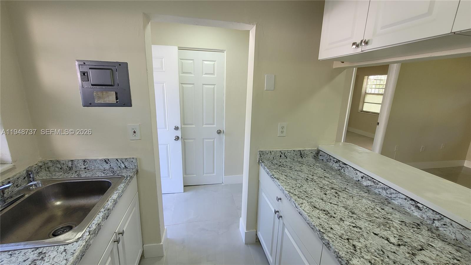 A kitchen features white cabinets, granite countertops, a stainless steel sink, and a doorway — 13240 Port Said Rd # 19, Opa-Locka FL 33054, OPA-LOCKA, FL