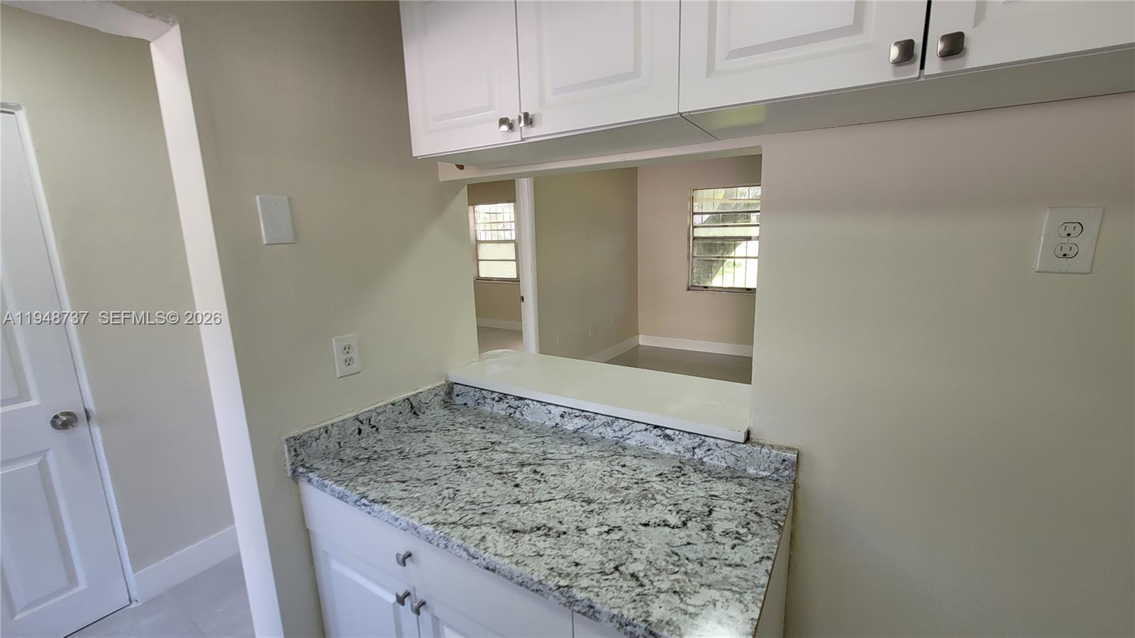 A kitchen pass-through window overlooks an adjacent room with white cabinets and granite countertops — 13240 Port Said Rd # 19, Opa-Locka FL 33054, OPA-LOCKA, FL
