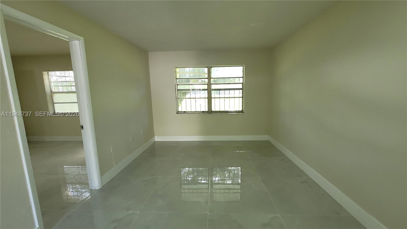 An empty room features light-colored tile flooring, beige walls, and two windows with security bars — 13240 Port Said Rd # 19, Opa-Locka FL 33054, OPA-LOCKA, FL