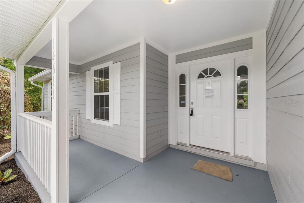 A covered front porch features gray siding, a white front door, and a white railing — 14611 NW 150TH LANE, ALACHUA, FL