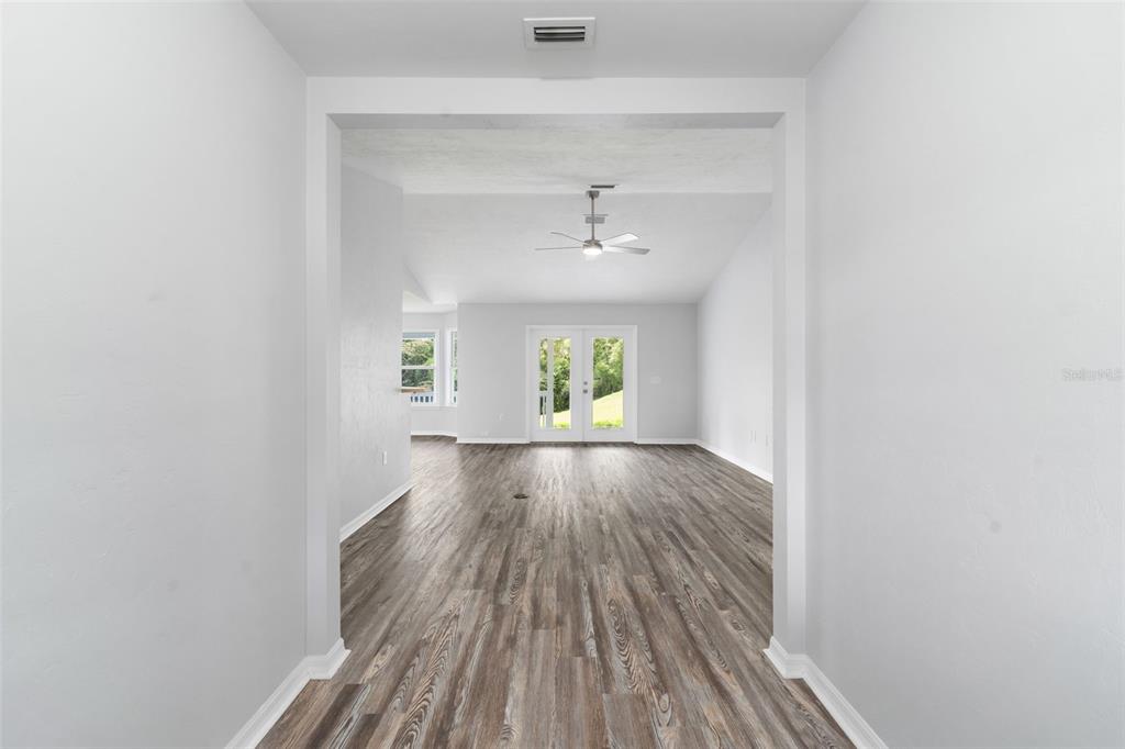 A view through a doorway into a living area with wood-look flooring and glass doors — 14611 NW 150TH LANE, ALACHUA, FL