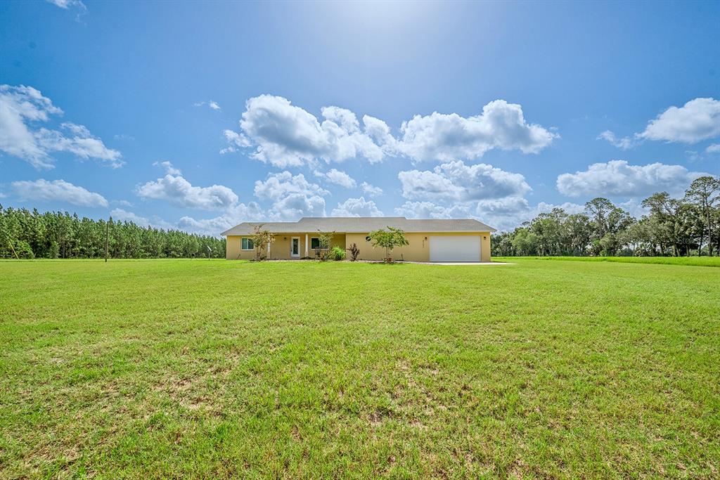 A single-story house with a garage sits in the middle of a large, grassy field — 4261 NW 57TH COURT, CHIEFLAND, FL