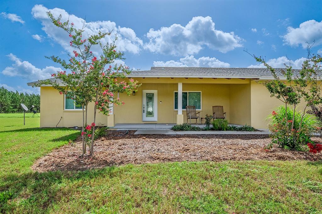 A yellow one-story house features a covered front porch, a glass-paneled door, and landscaping — 4261 NW 57TH COURT, CHIEFLAND, FL