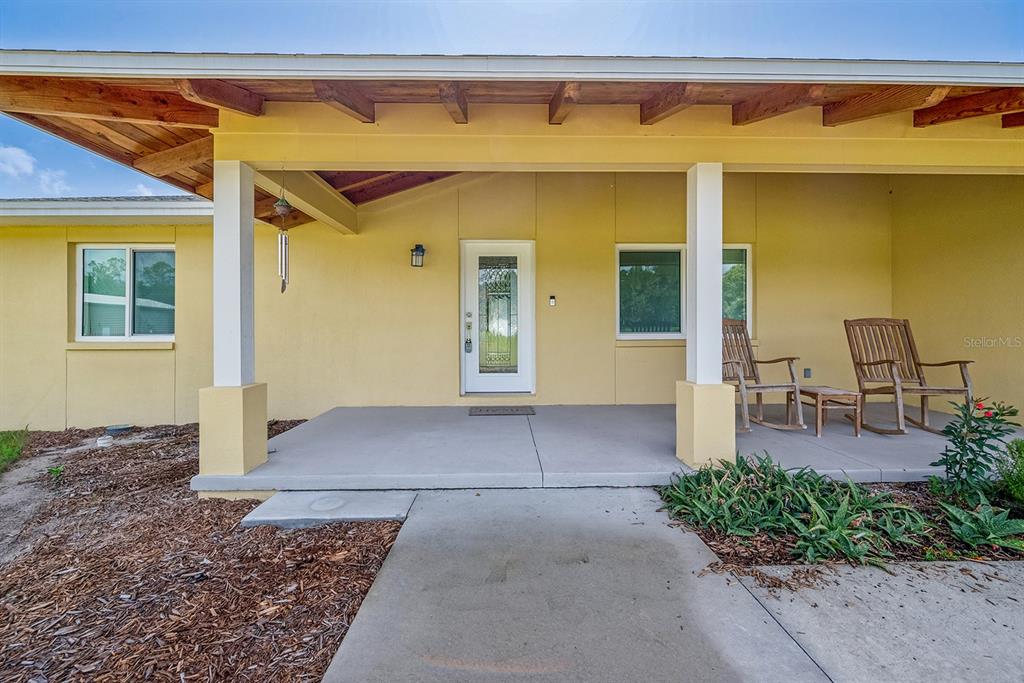 A yellow house exterior features a covered front porch with two wooden rocking chairs — 4261 NW 57TH COURT, CHIEFLAND, FL