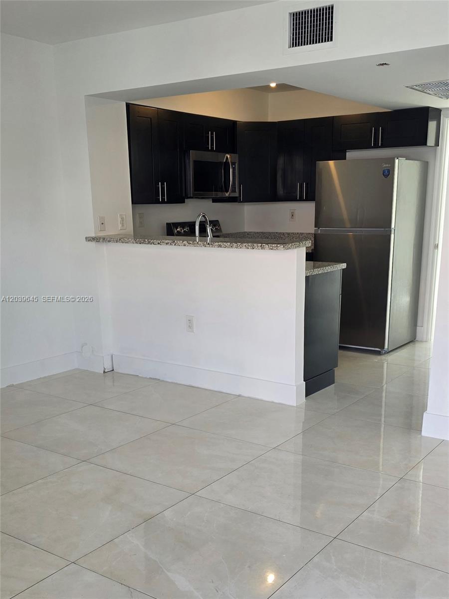 A kitchen features dark cabinetry, stainless steel appliances, granite countertops, and light tile flooring — 2154 W 60th St # 12111, Hialeah FL 33016, HIALEAH, FL