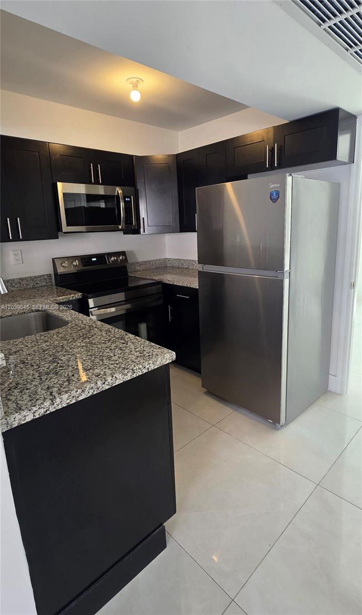 A kitchen features dark cabinets, granite countertops, and stainless steel appliances on a tiled floor — 2154 W 60th St # 12111, Hialeah FL 33016, HIALEAH, FL