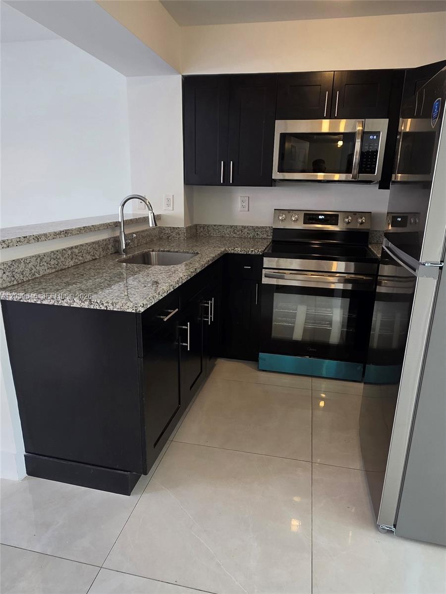 A kitchen features dark cabinets, granite countertops, stainless steel appliances, and light tile flooring — 2154 W 60th St # 12111, Hialeah FL 33016, HIALEAH, FL