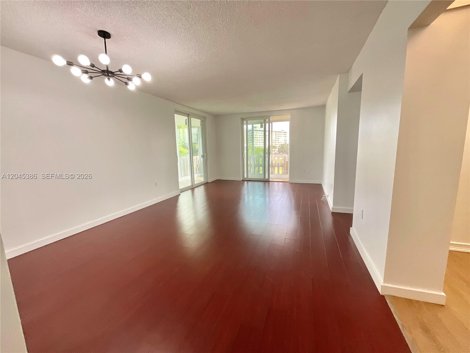 An empty living room features dark wood flooring, white walls, and a modern chandelier — 919 Hillcrest Dr # 302, Hollywood FL 33021, HOLLYWOOD, FL