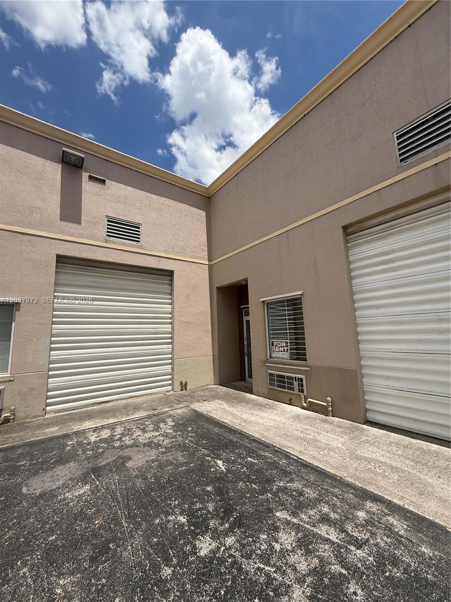 An exterior view of a commercial building featuring two roll-up doors and a central entrance — 15075 SW 137th St # 14, Miami FL 33196, MIAMI, FL