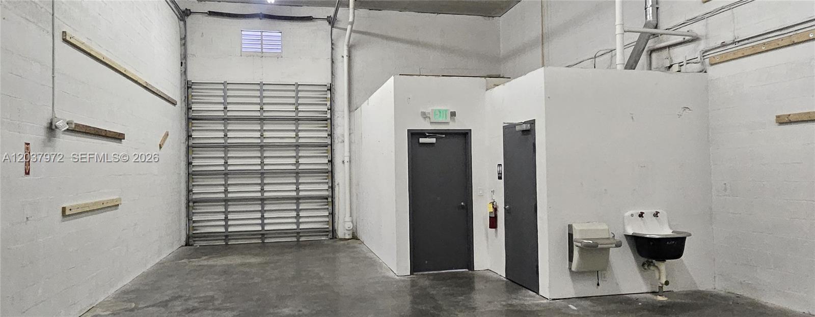 An industrial warehouse space features a roll-up door, two gray doors, and a utility sink — 15075 SW 137th St # 14, Miami FL 33196, MIAMI, FL