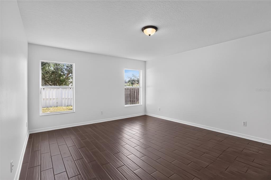 An empty bedroom with white walls, dark wood-look tile flooring, and two windows — 2079 NEWTOWN ROAD, GROVELAND, FL