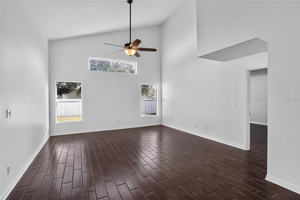 An empty living room with vaulted ceilings, dark wood-look flooring, and several windows — 2079 NEWTOWN ROAD, GROVELAND, FL