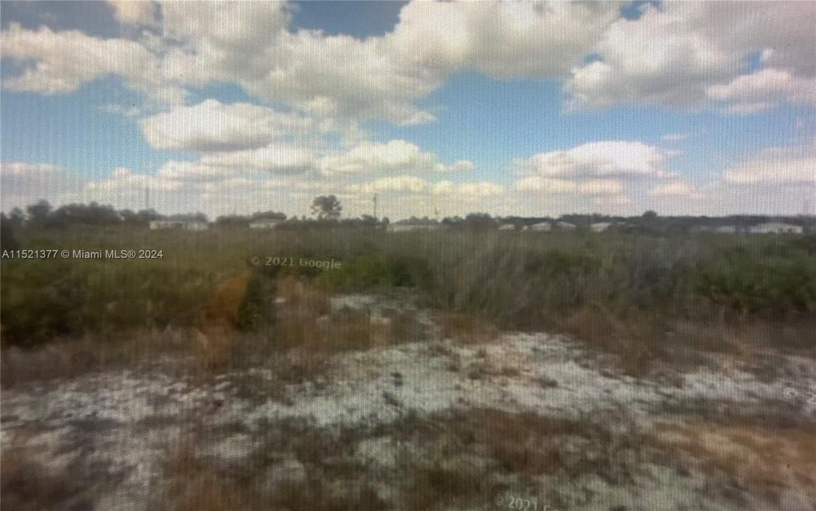 This is an exterior view of a flat, undeveloped grassy lot under a cloudy sky — 2902 W 72ND ST, Lehigh Acres FL 33971, LEHIGH ACRES, FL