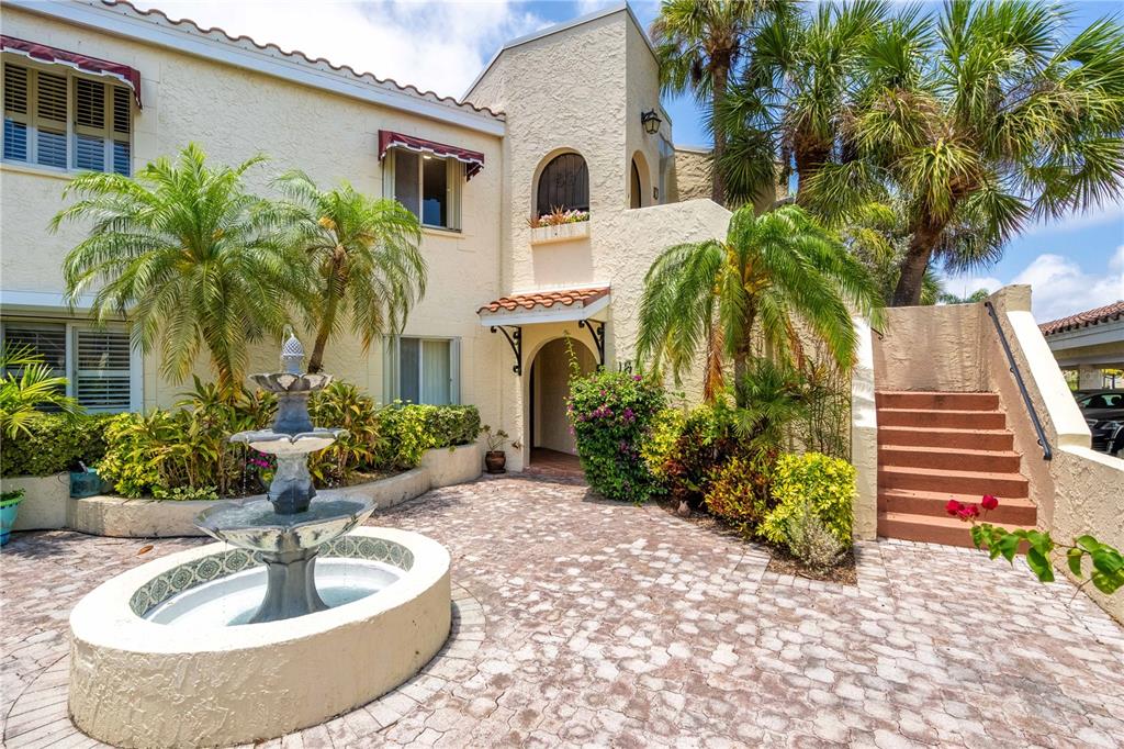 A multi-story stucco building features a tiered fountain in a paved courtyard with palm trees — 6101 34TH STREET W UNIT 1D, BRADENTON, FL