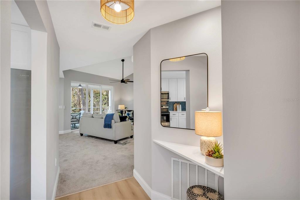 A hallway with a mirror and console table leads into a living room with carpet — 6101 34TH STREET W UNIT 1D, BRADENTON, FL
