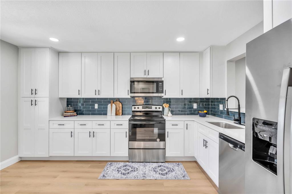 A kitchen features white cabinets, stainless steel appliances, and a blue subway tile backsplash — 6101 34TH STREET W UNIT 1D, BRADENTON, FL