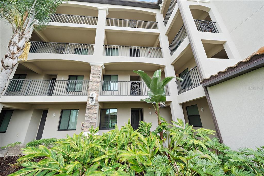 A multi-story apartment building exterior features balconies with metal railings and lush tropical landscaping — 16814 VARDON TERRACE UNIT 106, BRADENTON, FL