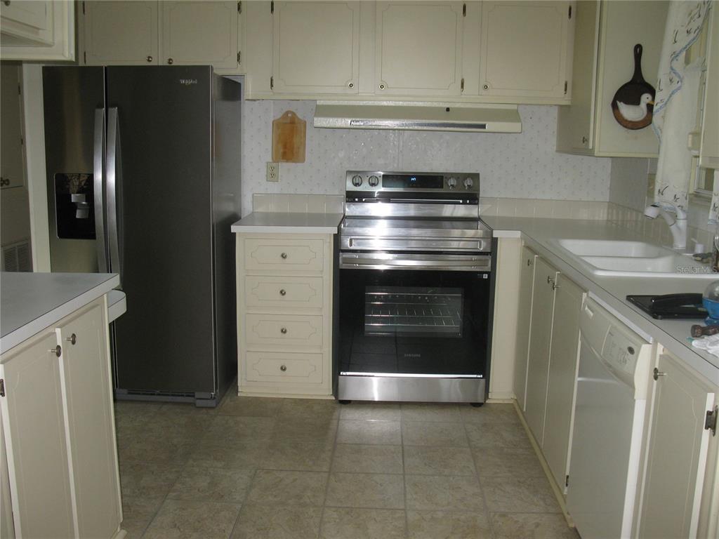 A kitchen features off-white cabinets, a stainless steel refrigerator, a range, and a dishwasher — 356 MELBOURN DRIVE, HAINES CITY, FL