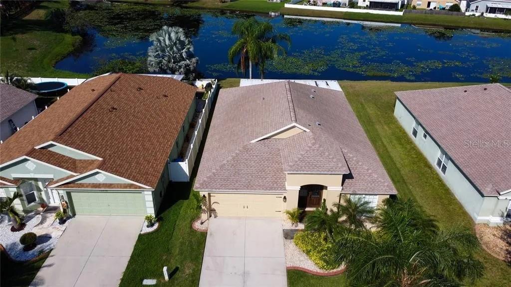 An aerial view shows two suburban houses with beige and green exteriors beside a pond — 12213 RAVENS NEST PLACE, RIVERVIEW, FL